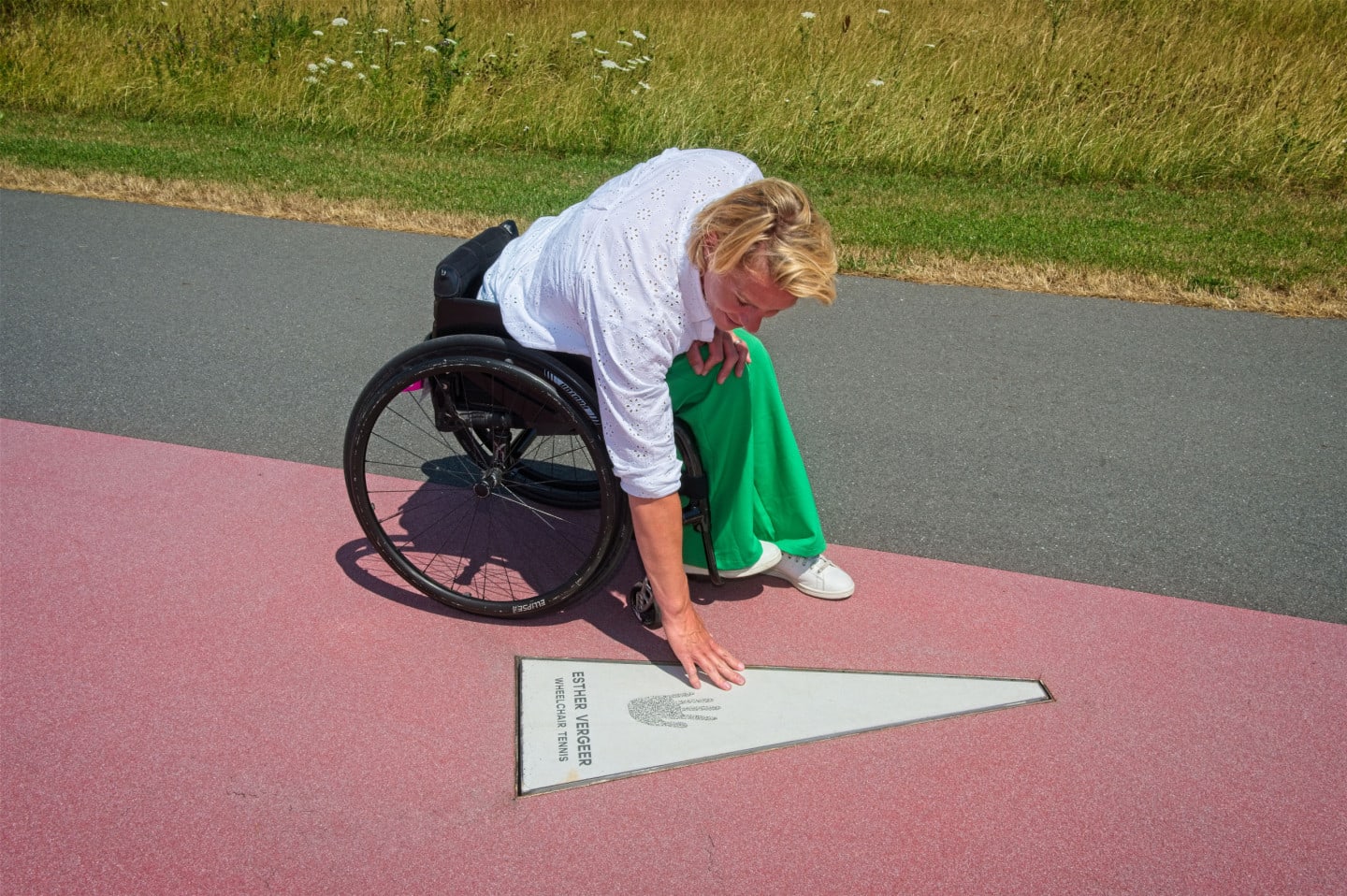 Woman in wheelchair holding her hand to her hand print in the concrete at adidas.