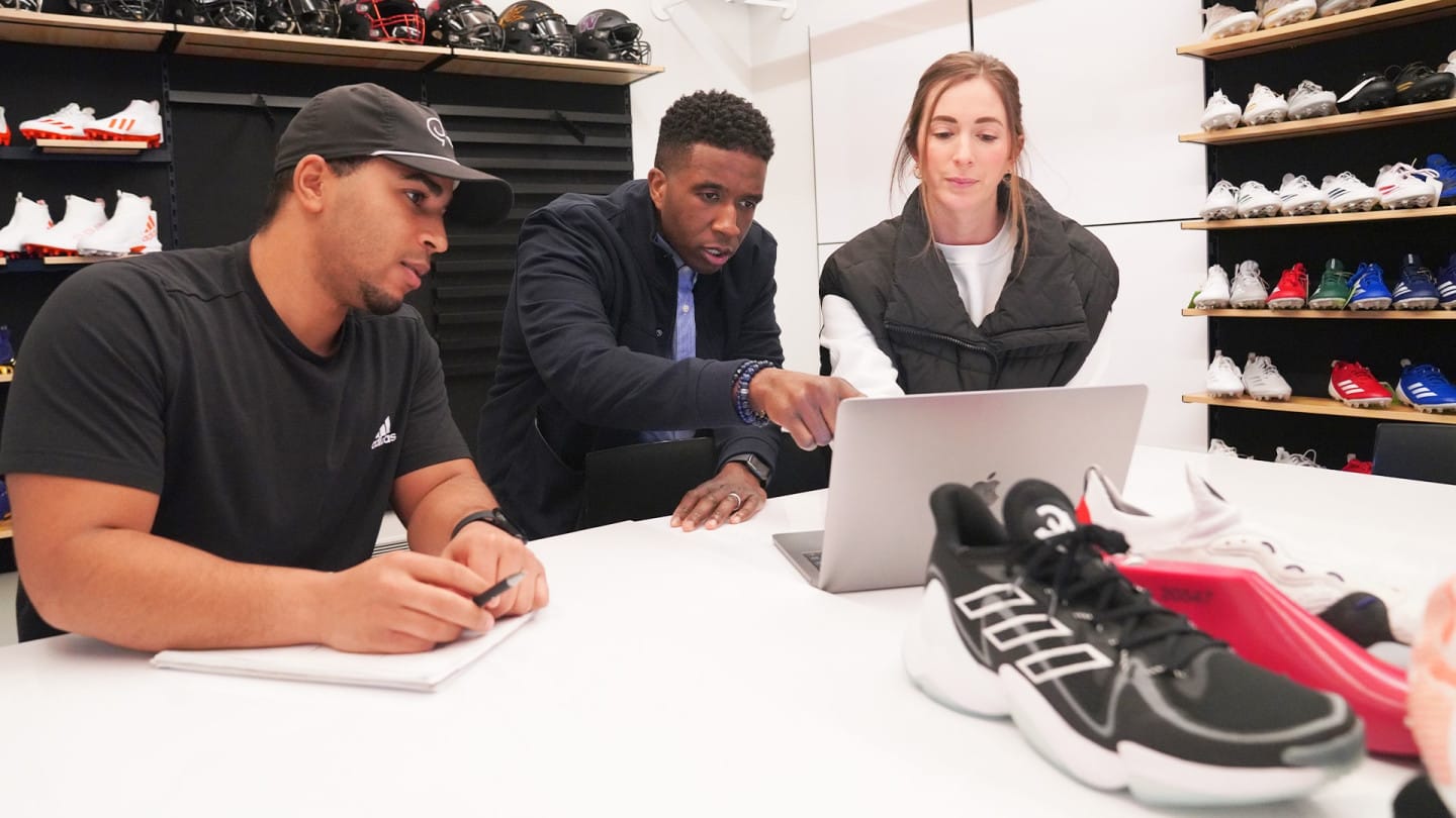 Three adidas employees working together while looking at a laptop.
