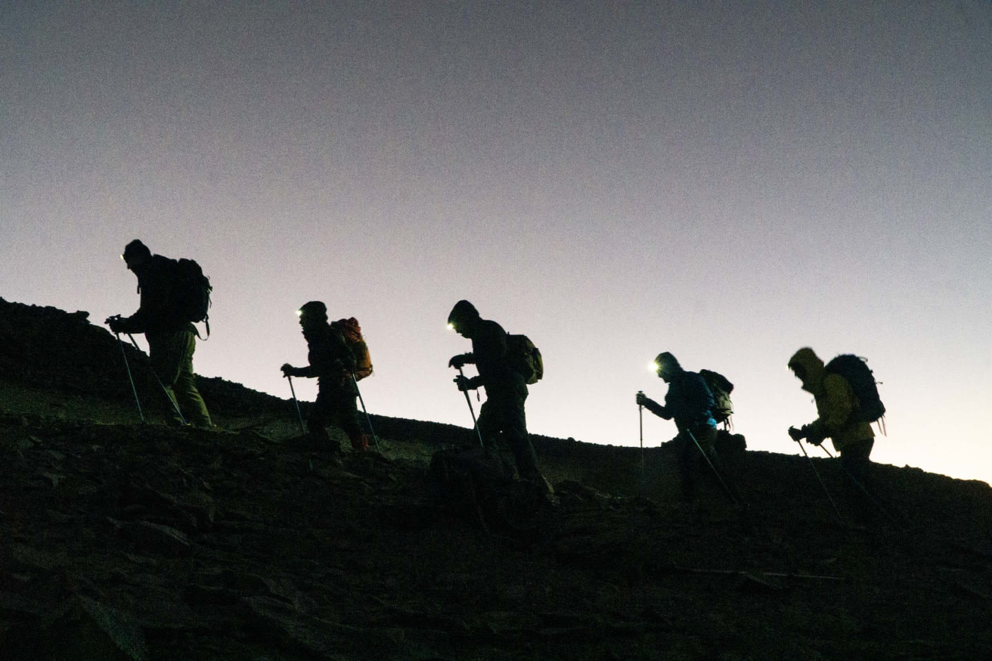 Hikers walk in line up a mountain in the dusk.