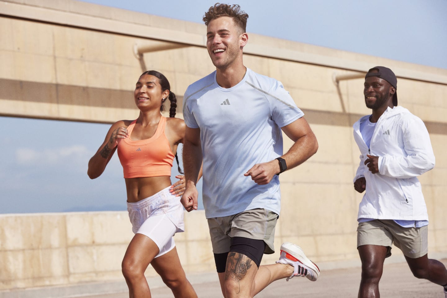 Three people run together with concrete structure in the background.