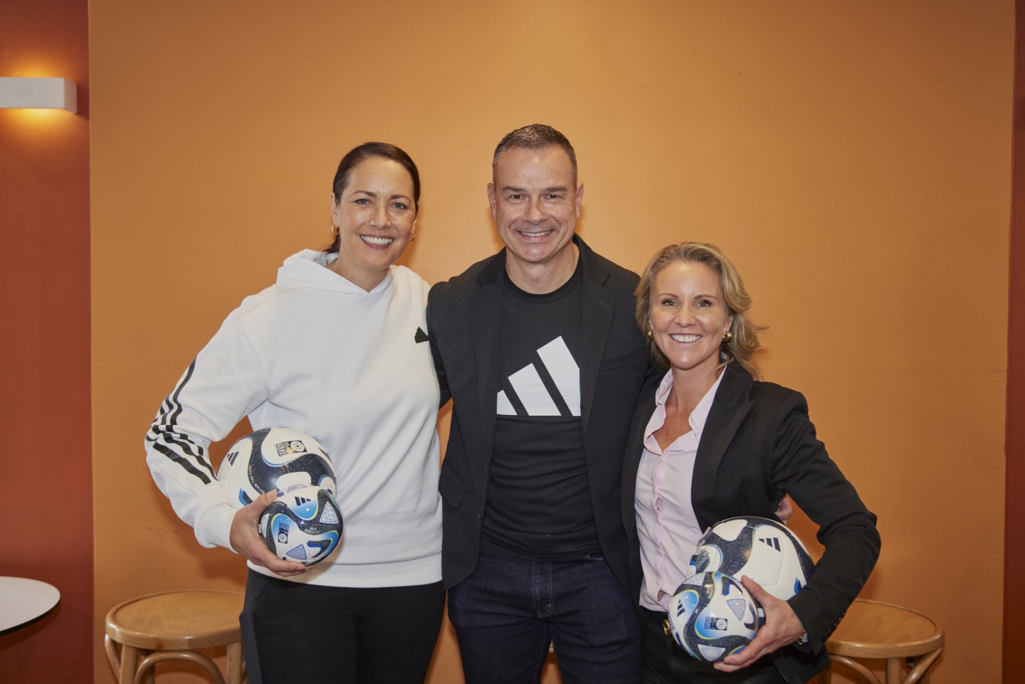 Three people stand together holding adidas footballs.
