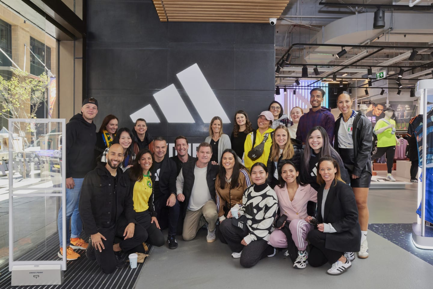 A big group poses in front of a three stripes sign.