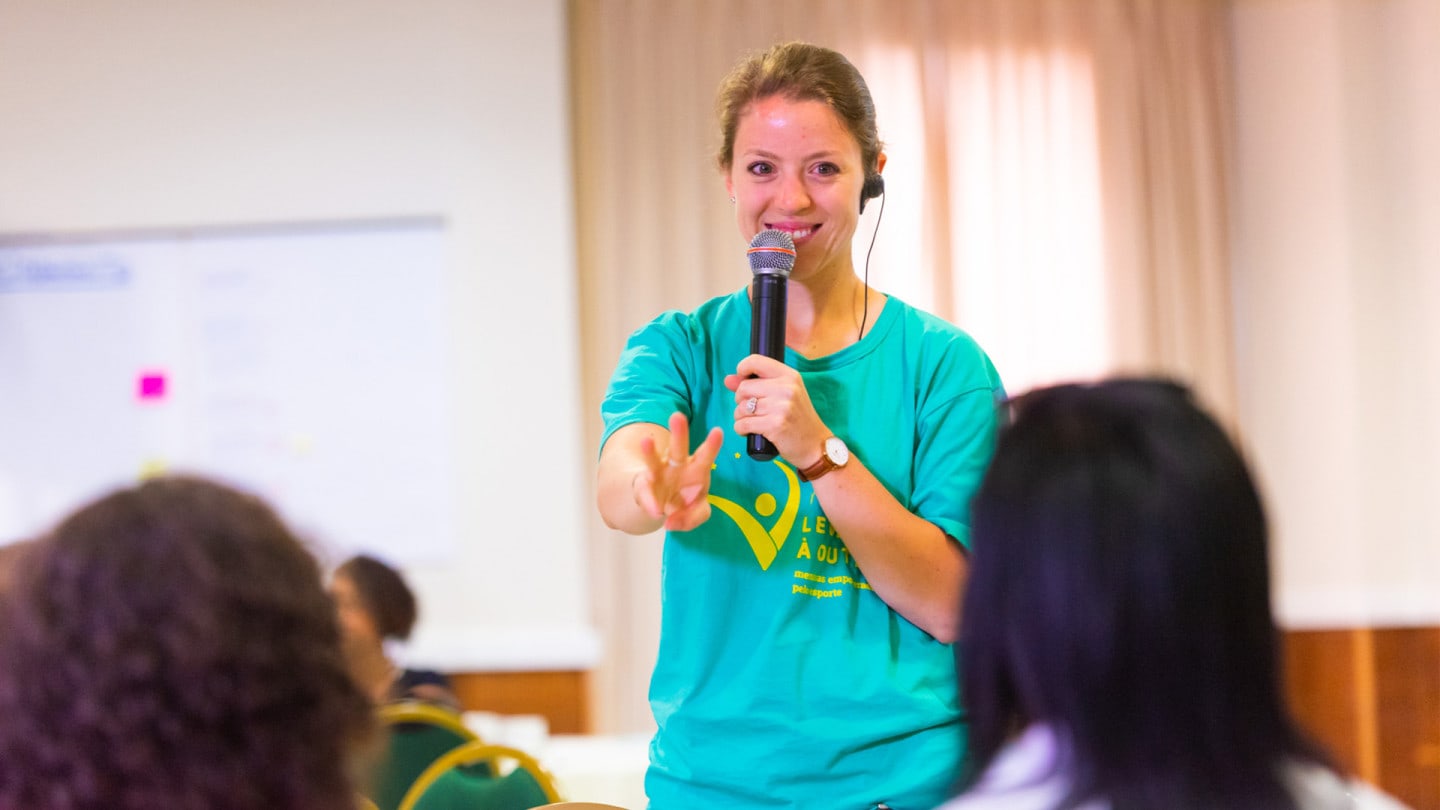 A woman holds a microphone while giving a talk.