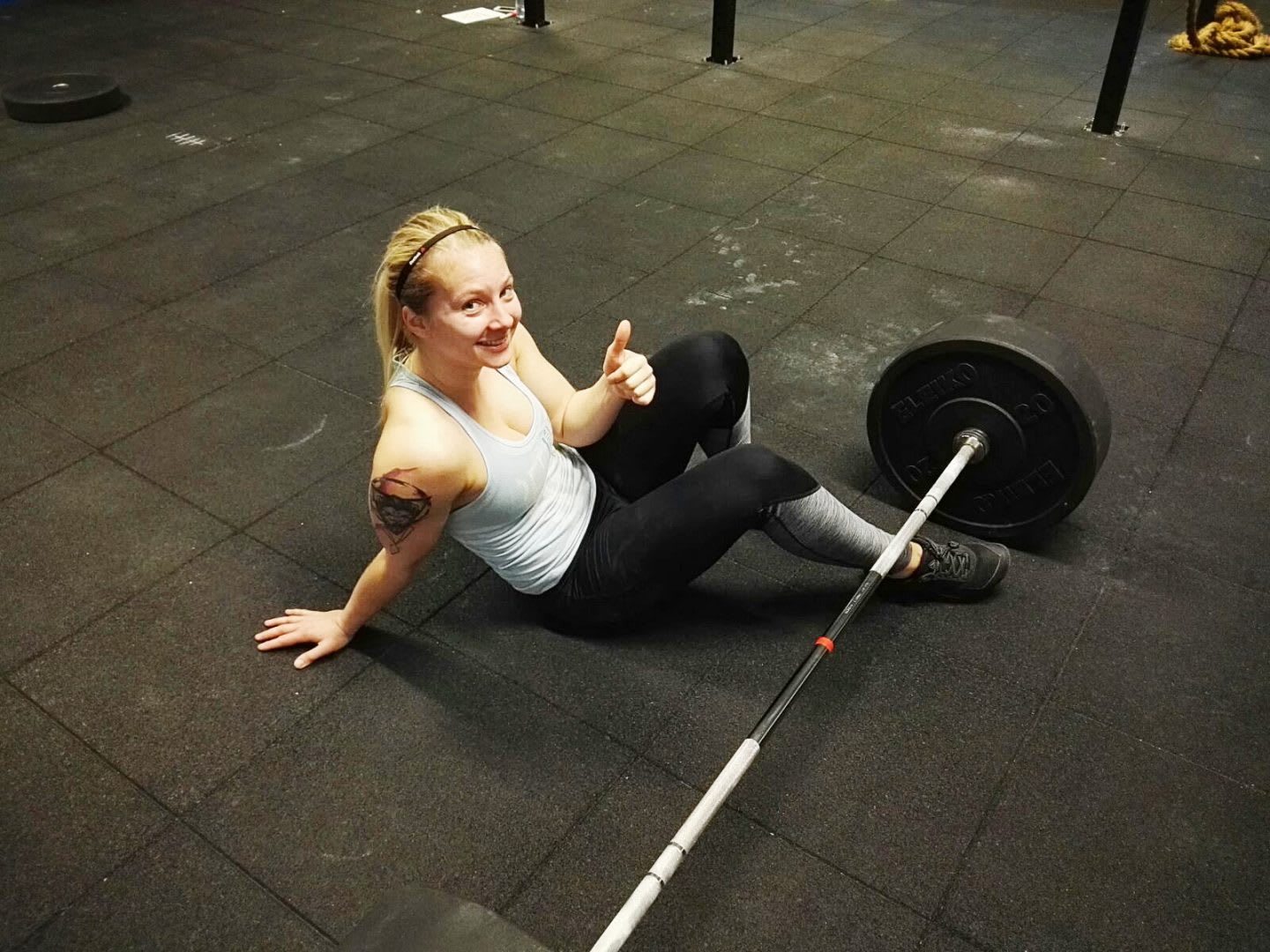 CrossFit girl sitting on the ground next to a barbell showing a thumbs up self-confidence letter to your haters training