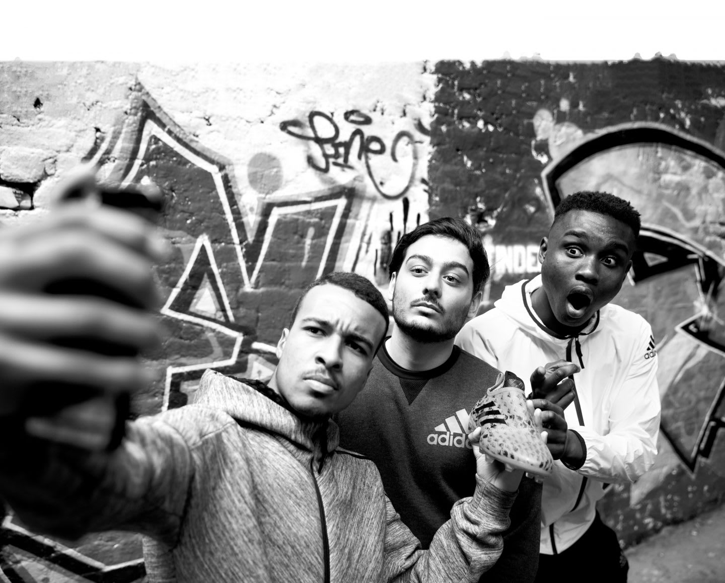 three young men taking selfie in front of graffiti wall london football players glitch creators