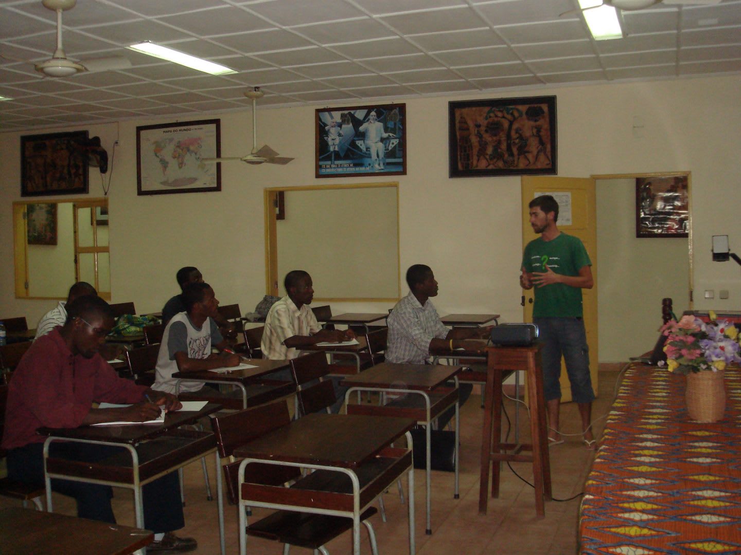 Portuguese guy holding is standing in a class room and gives a presentation in front of African school children.