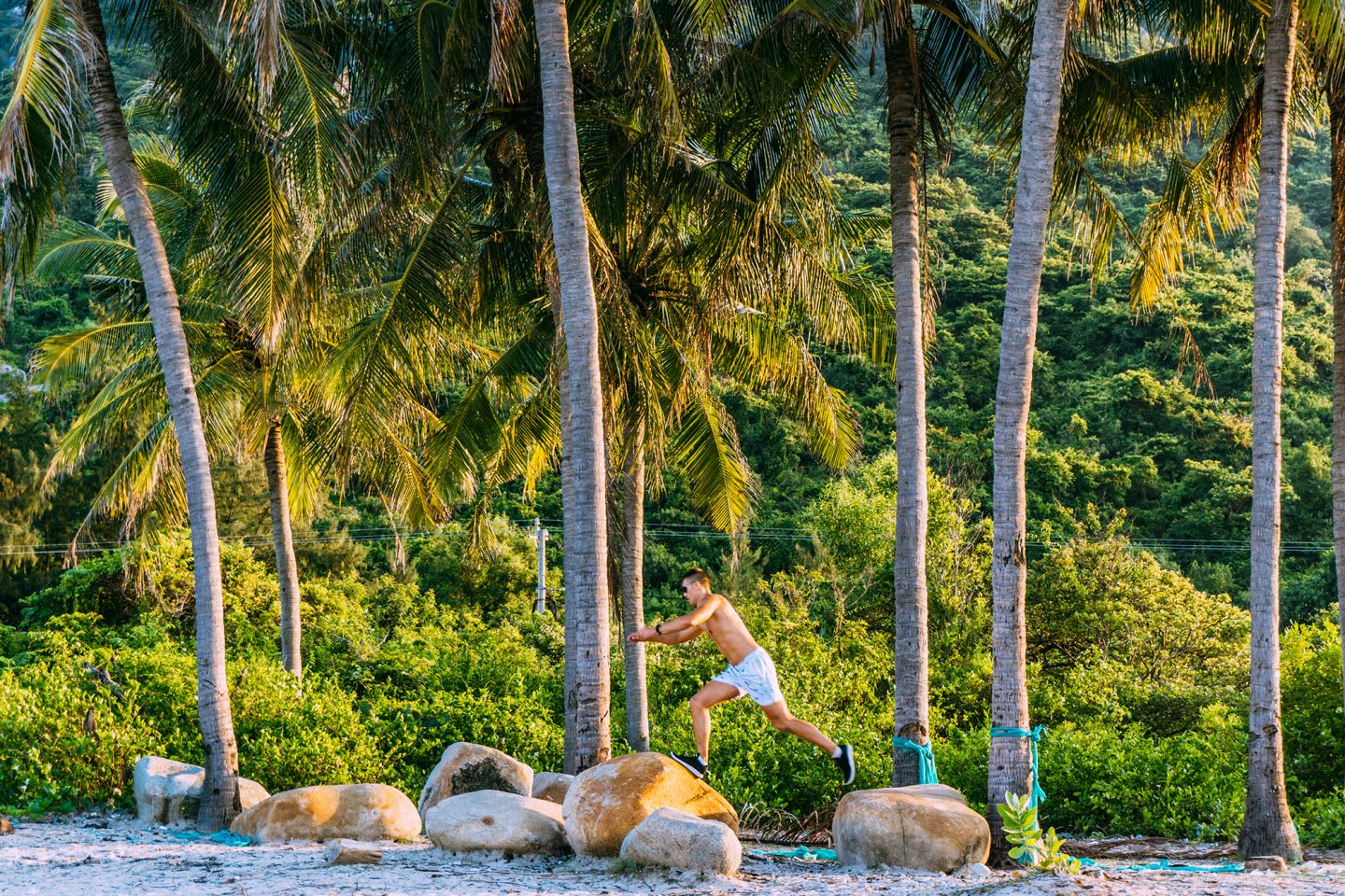 Man running and jumping from rock to rock at a beach. In the background one can see huge palm trees.