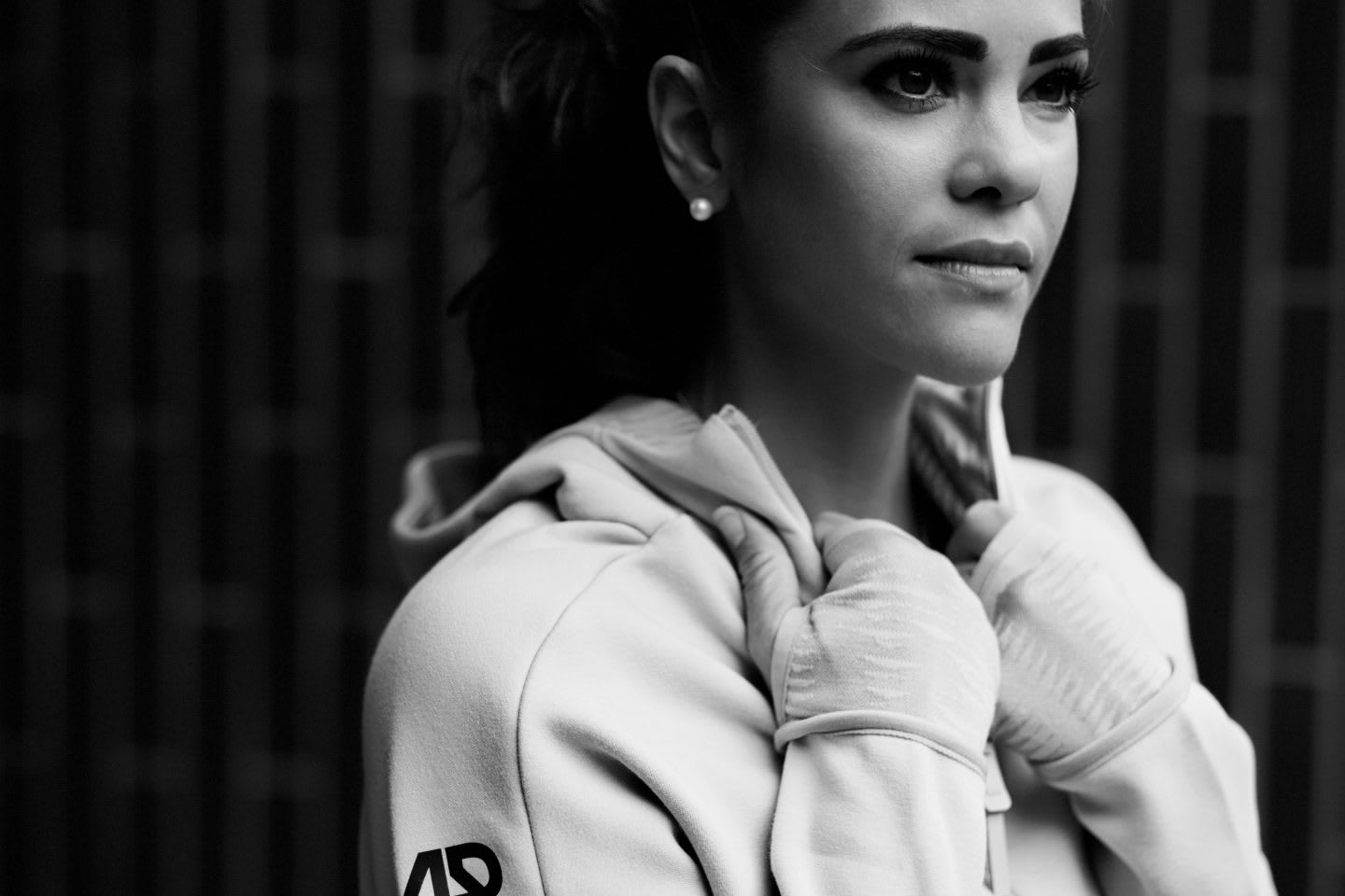 Black and white picture of a woman wearing a white adidas Runners track top and standing in front of black background, Laura Hilber_adidas Runners_GamePlan A