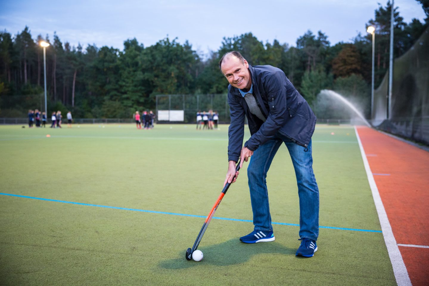 Coach is smiling at the camera while demonstrating a proper field hockey stance with the stick and ball.