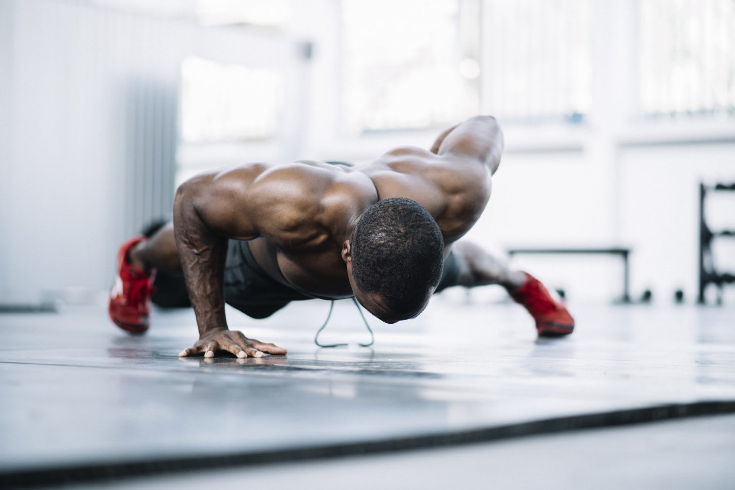 A shirtless man in a gym is doing a one armed push-up.