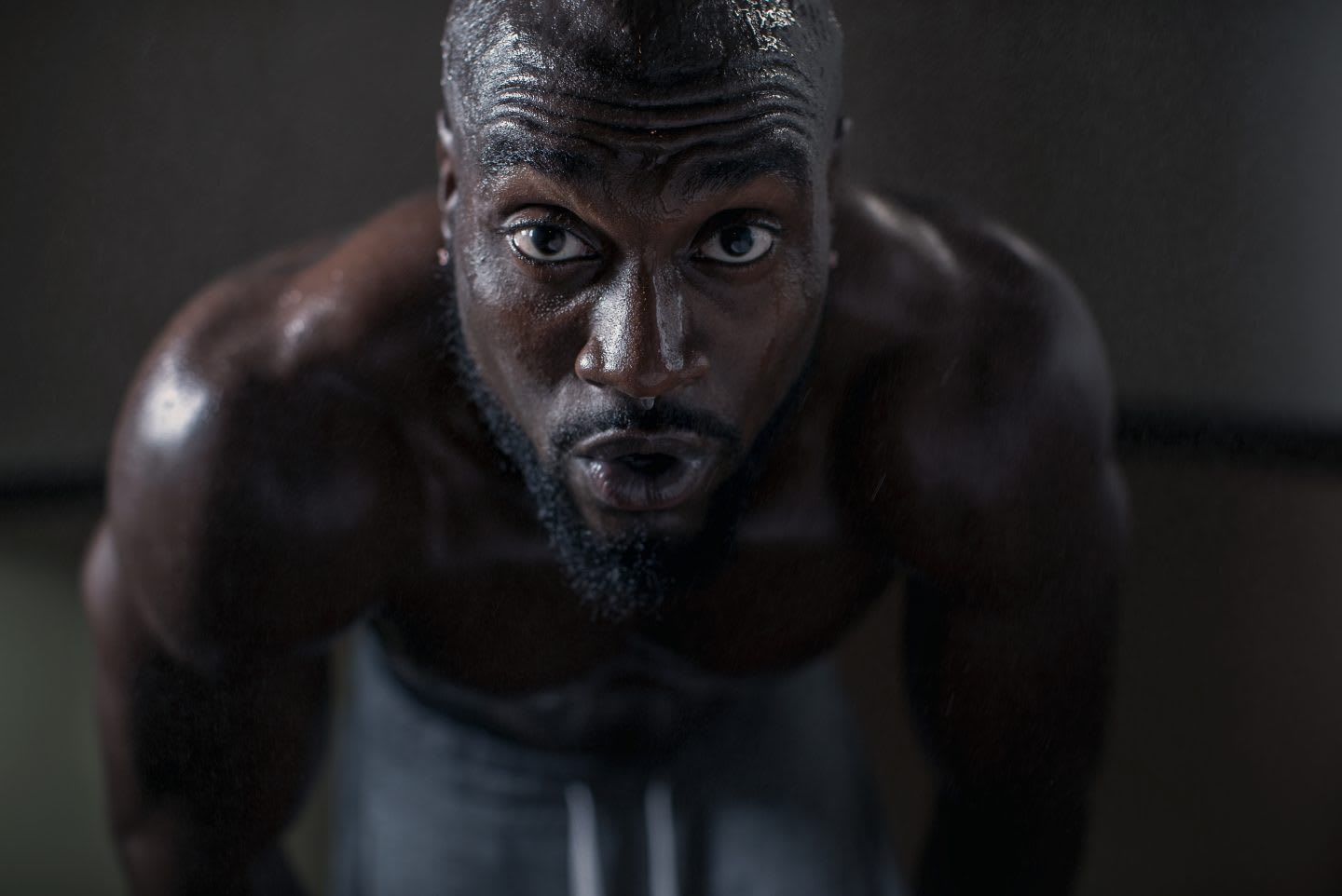 A man is looking deeply into the camera while exhaling during a strength workout.