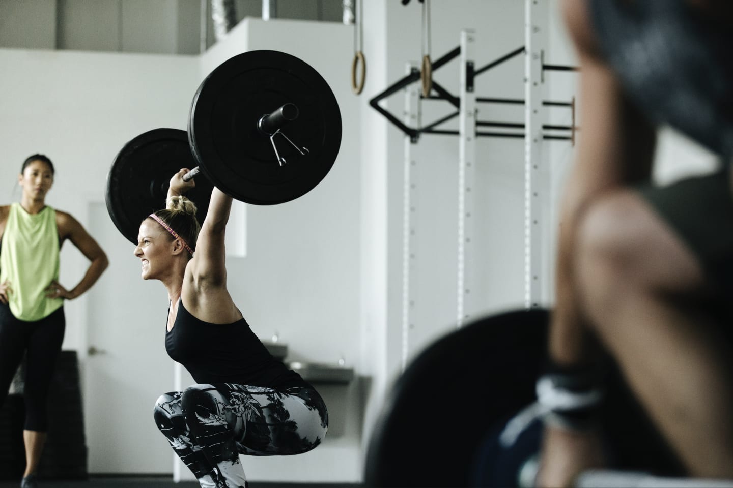 Woman lifting weight with another woman watching in the background.