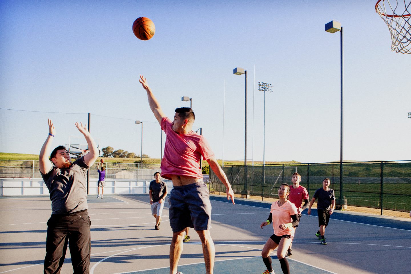 A group of men is playing basketball outside in the sun. Team; Motivation; Training; Competition; Success; Dedication; Teamwork