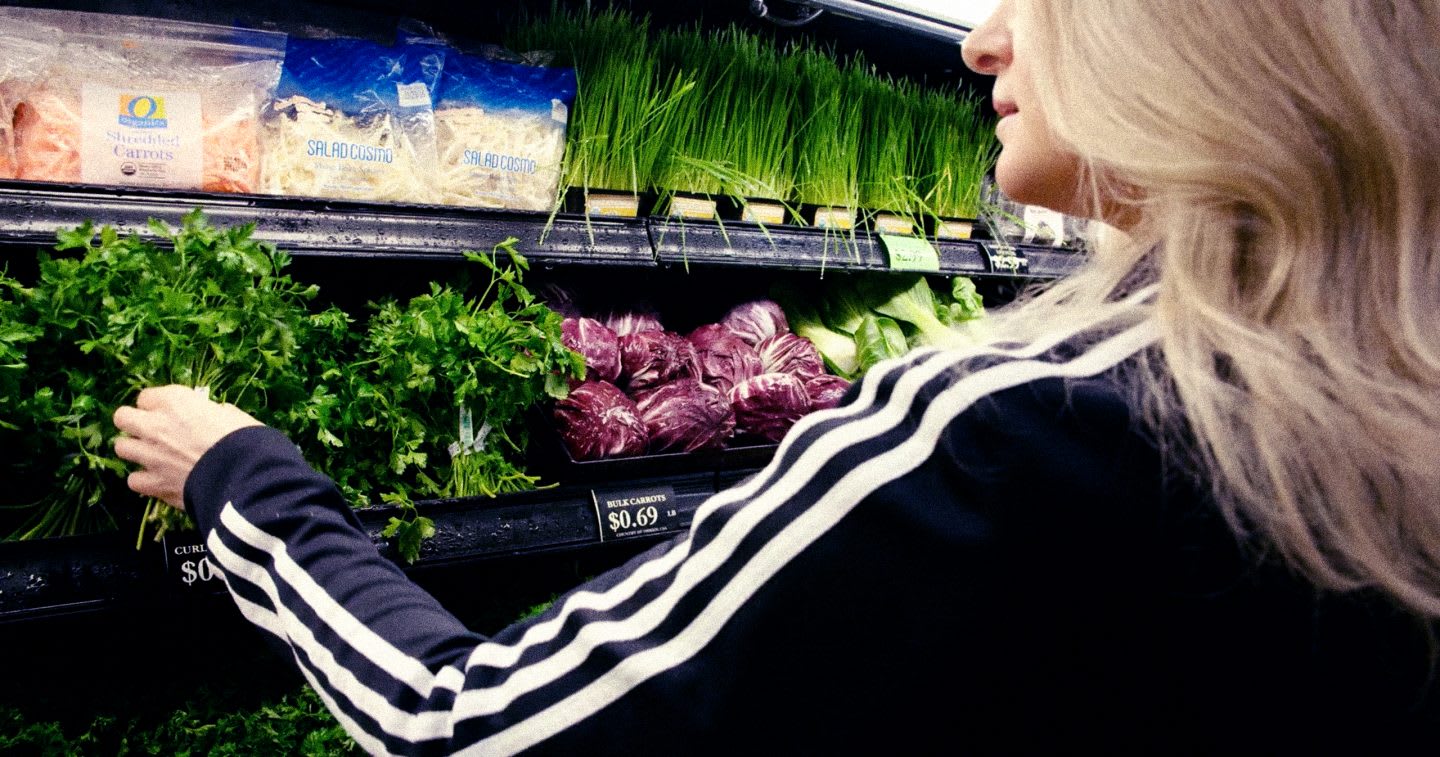 Blonde woman in a black adidas sweater with three stripes buys cilantro