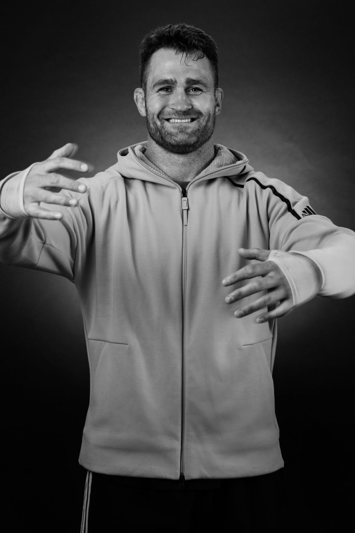 Black and white of rugby player James Horwill holding his arms in the position of a hug.