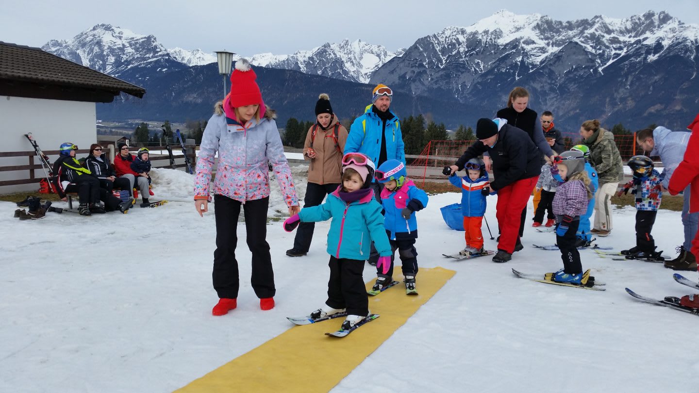 A skiing class is getting an instruction with mountains in the background