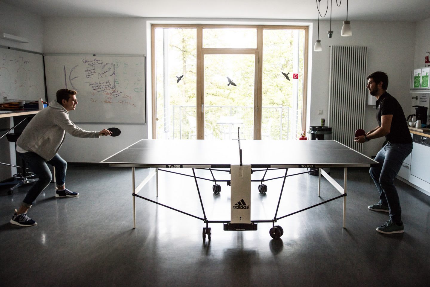 Two colleagues play a round of table tennis inside before starting their work day.