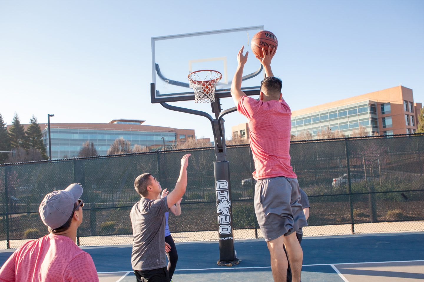 Four men play basketball in a basketball court and one of the men jumps in the air to make a shot. basketball, team, team sport, sport, hobby.