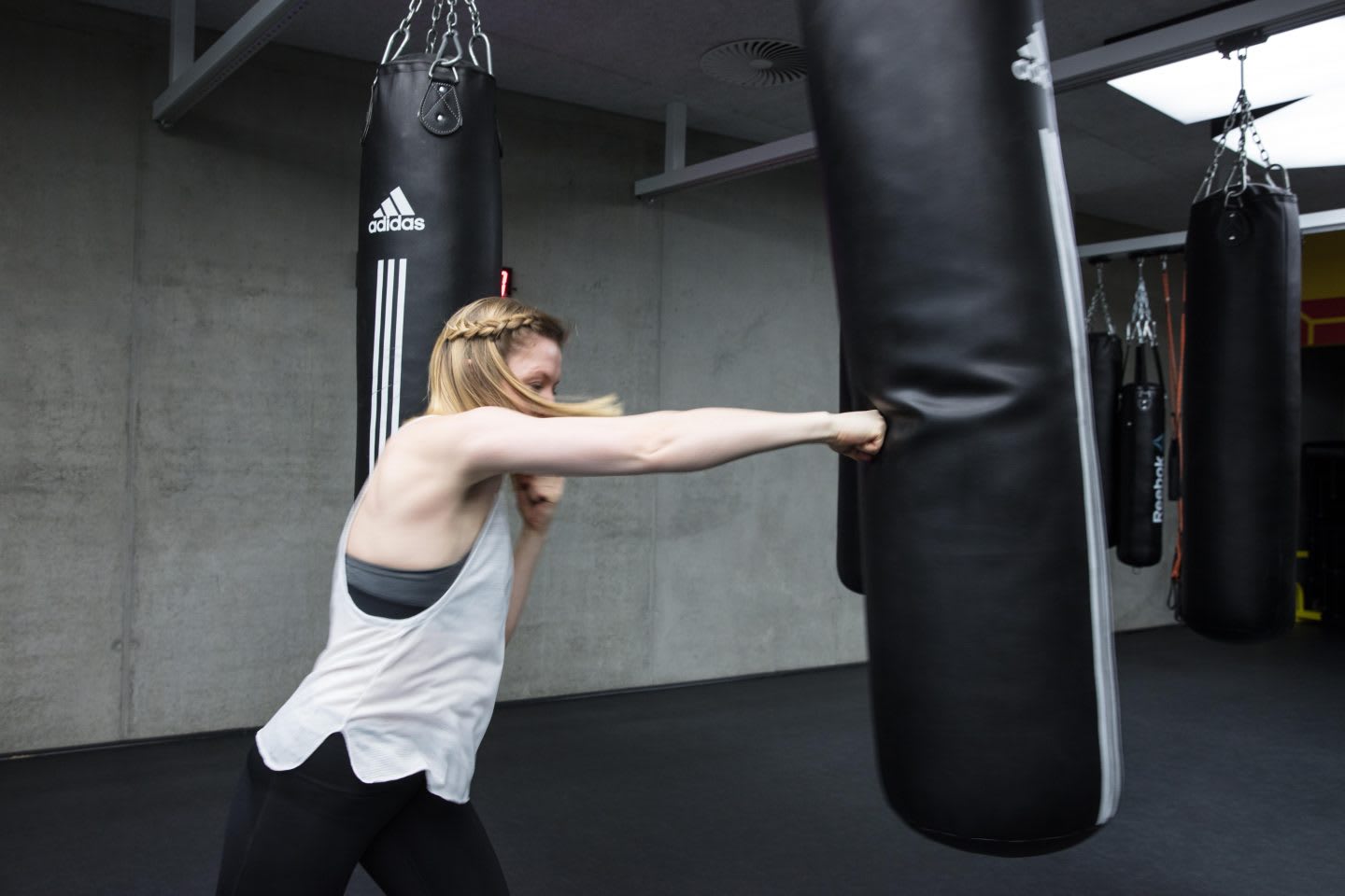 A young woman punches a boxing bag in a gritty gym. martial arts, power, strength, fitness, gym, workout