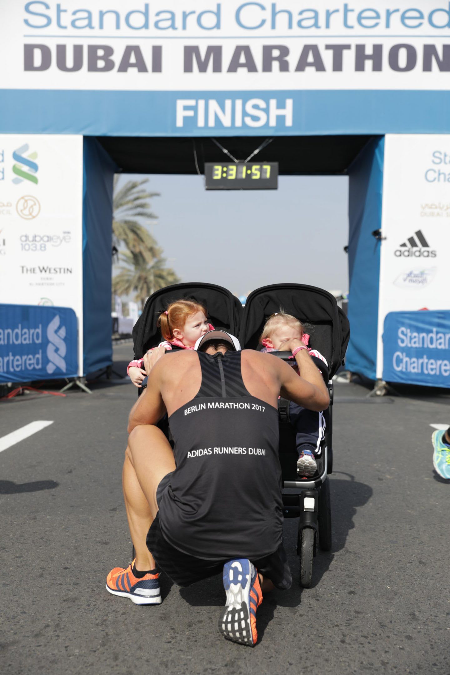 A father kneels down infront of his daughters after finishing a marathon. running, marathon, completion, success, goal, happy, proud