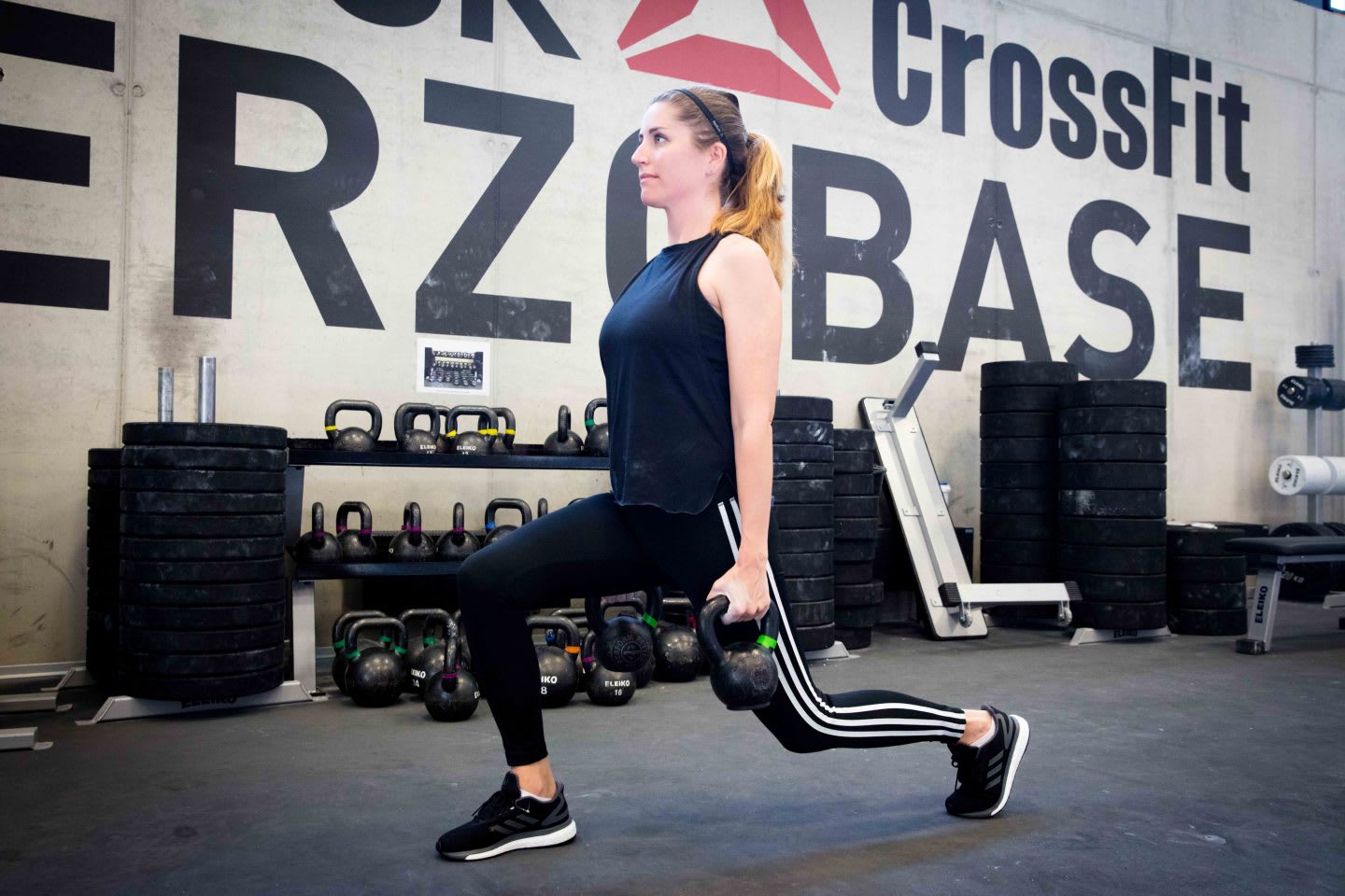 Woman holding kettle bells while doing lunges in a CrossFit box. adidas, GamePlan A, work life, health, lifestyle