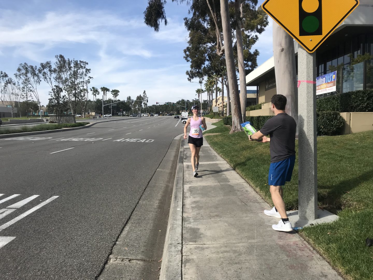 A female runner runs along the street where a supporter holds out a bottle of water for her. support, running, runner, determination
