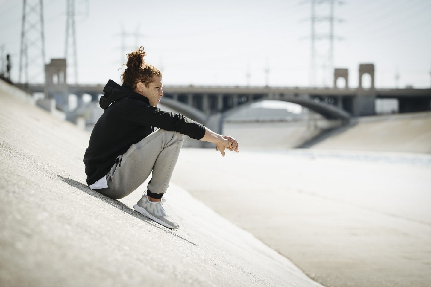 Guy wearing sports clothes sitting on concrete ramp with bridge in the backgruond, urban, urban athlete, workout, after workout, recovering, overview, take a breath, Reebok, GamePlan A