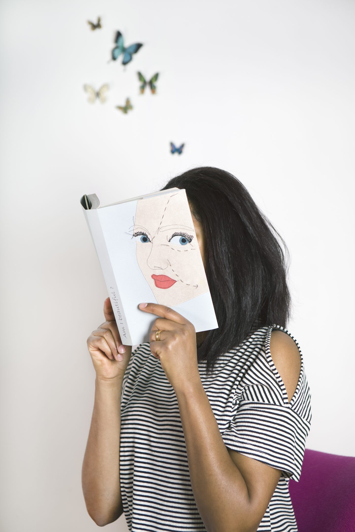 Woman wearing a stripy shirt reading a book with face hidden, imagination, butterflies, thinking, creative, personal, rest, inspiration, GamePlan A