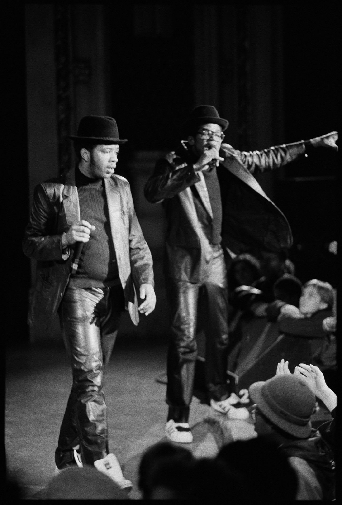 Run DMC perform on stage wearing their superstars. The image is black and white and the performers are facing the crowd with arms in the air.