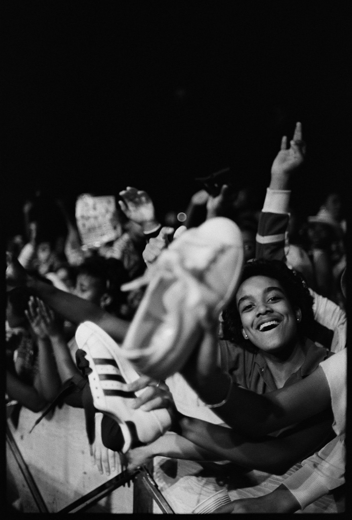 Fans at a Run DMC concert watch the show with their hands in the air and holding up their adidas Superstars.