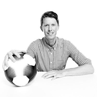 Man wearing a checked shirt posing with football in right hand, James Bean, adidas, employee