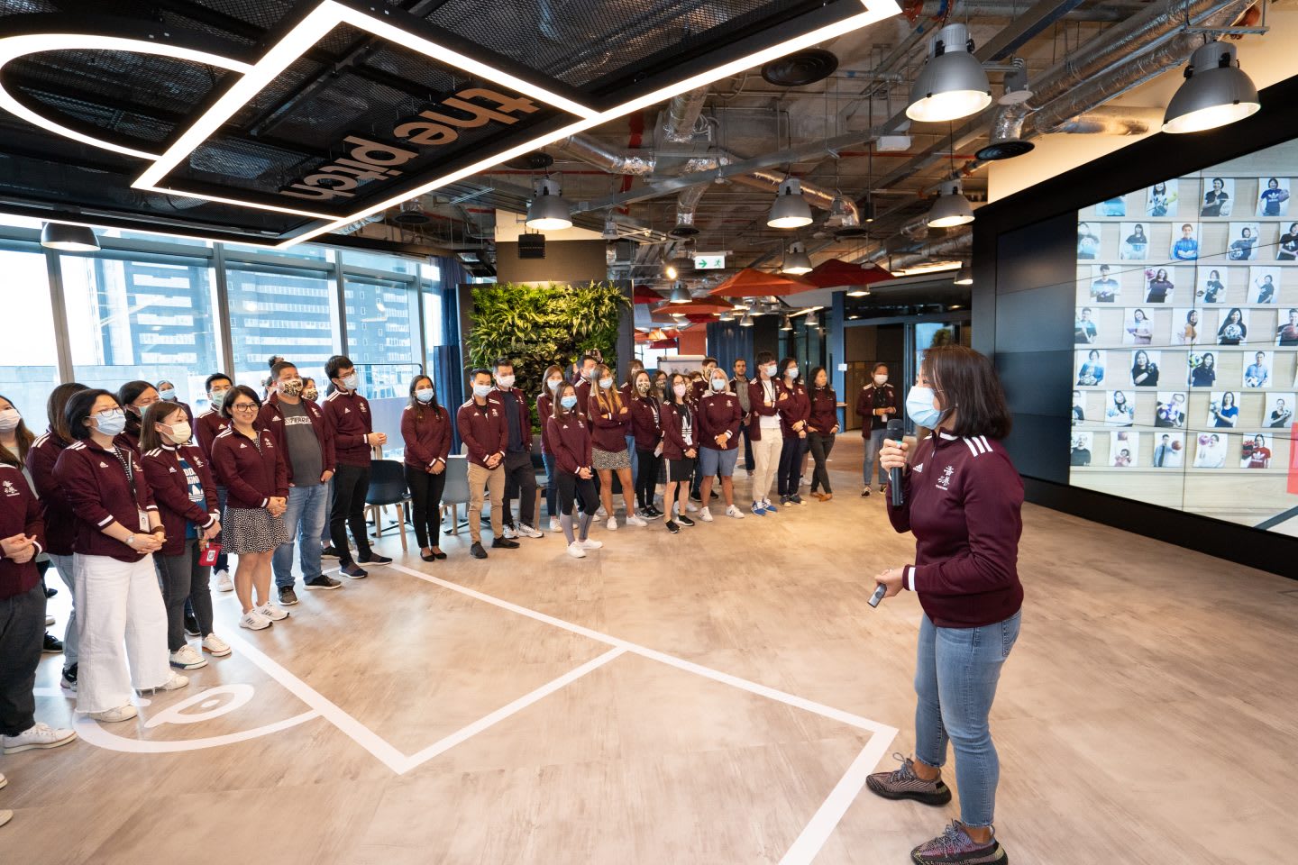 Women wearing medical mask and maroon jacket holding a microphone and giving speech in front of crowd, Hoa Ly, adidas, employees, Sourcing, women