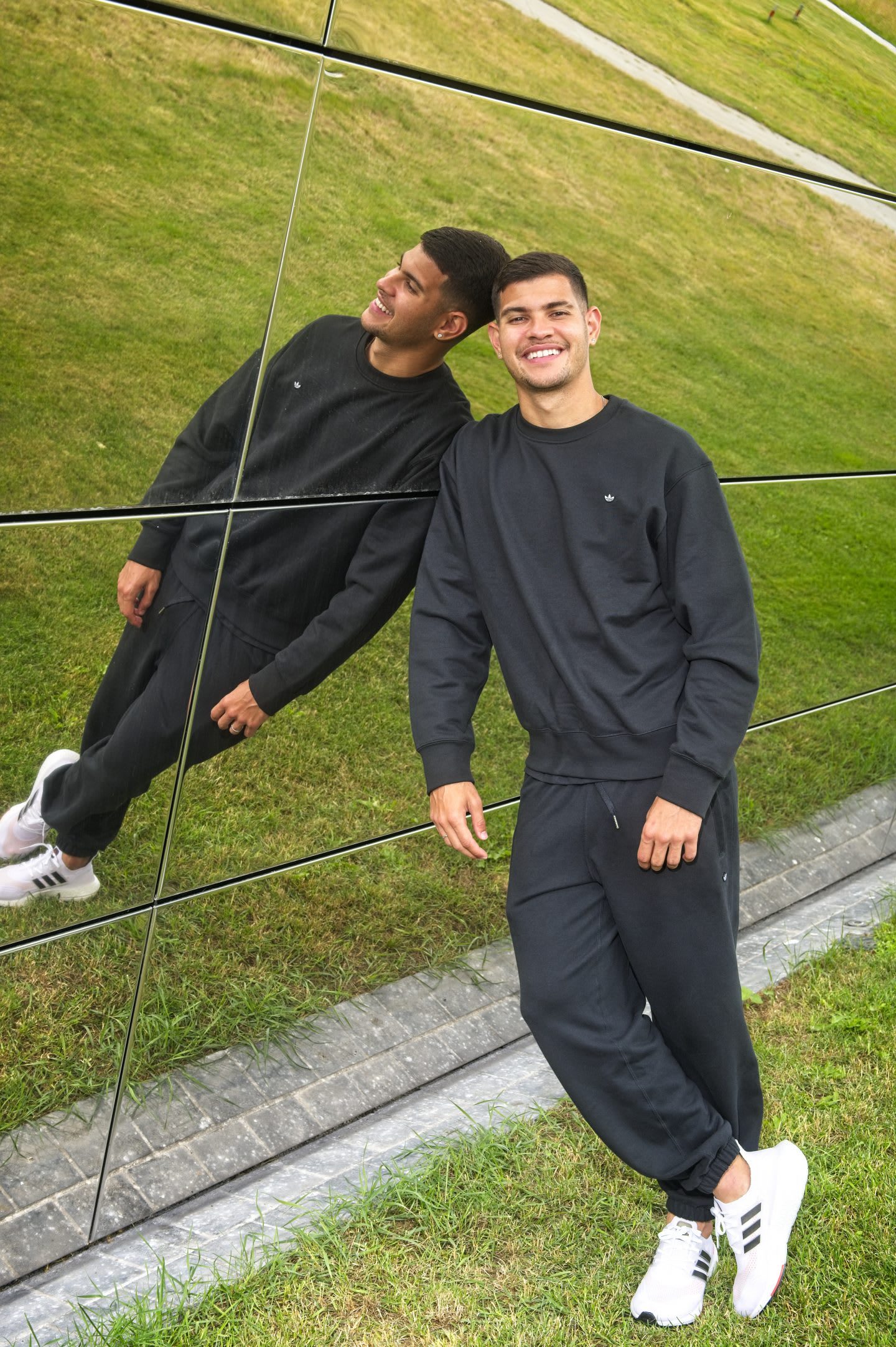 Bruno Guimaraes leaning on a wall of a building. Bruno Guimaraes, smile, Lifestyle, mindset, goals, humble, football, adidas