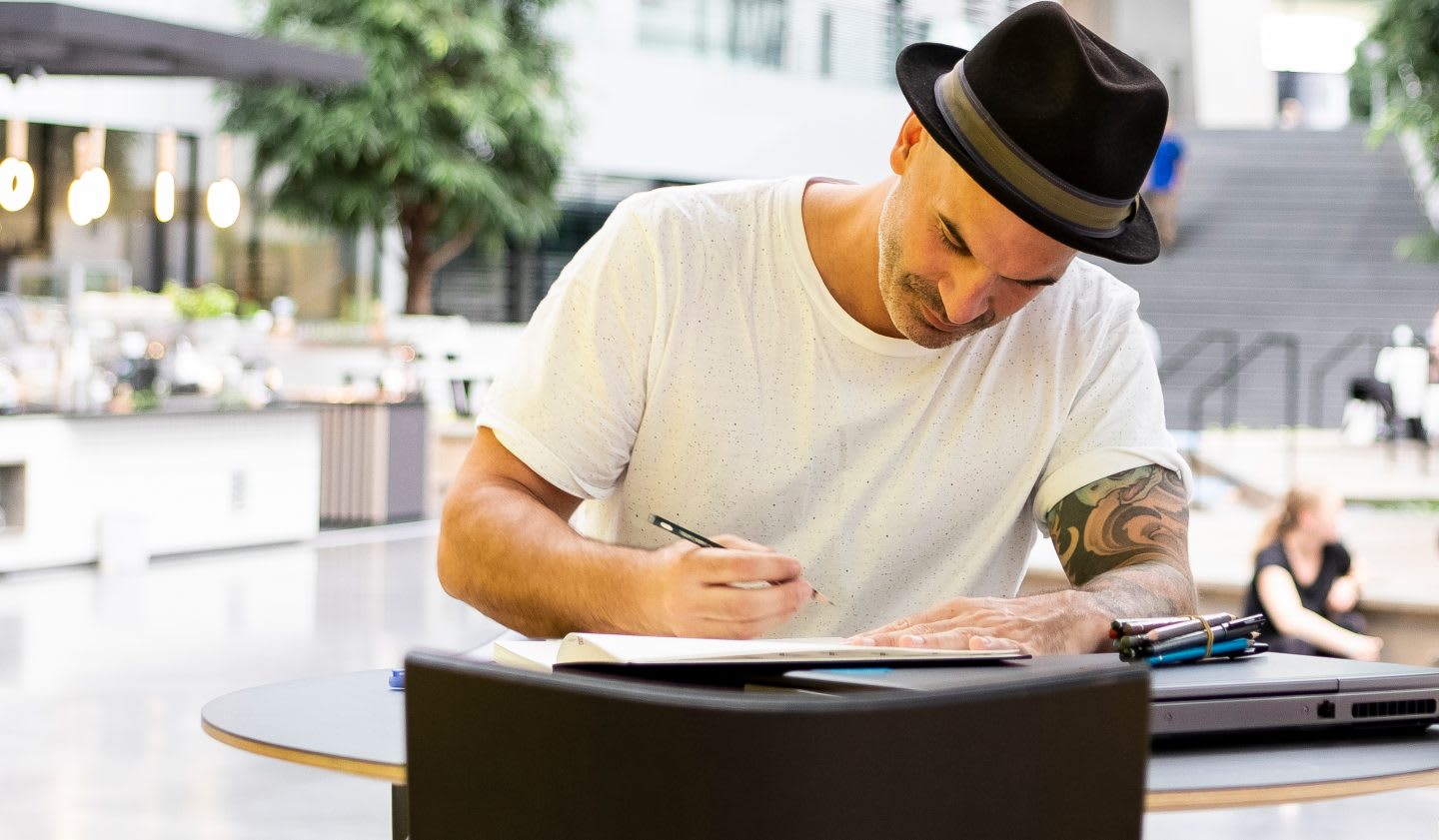 Man wearing hat and white t-shirt writing in notebook, employee, adidas, HQ, worklife