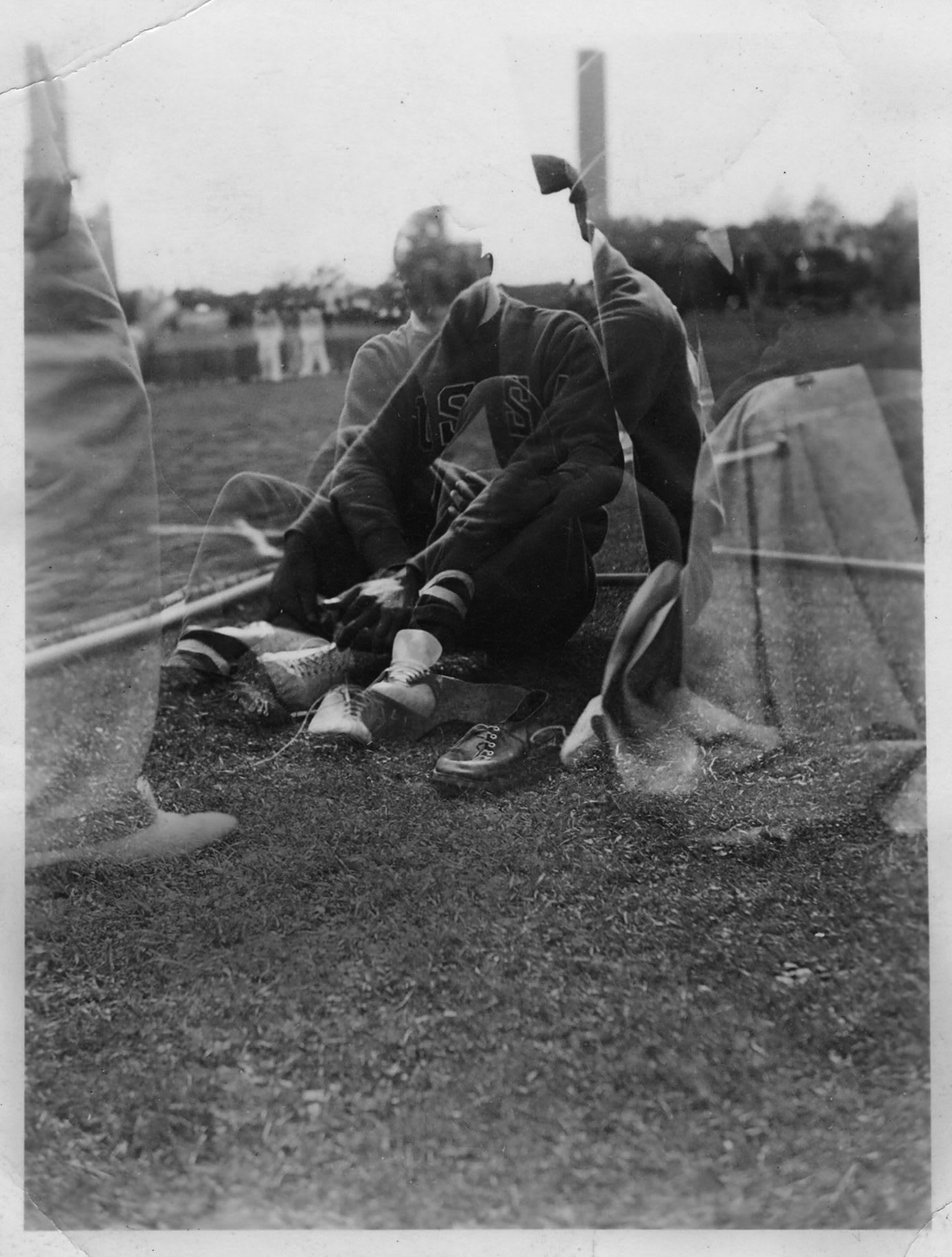 Black-and-white photograph of man putting on shoes on the ground, Jesse Owens, Berlin, adidas, Adi, Dassler, sports, sport