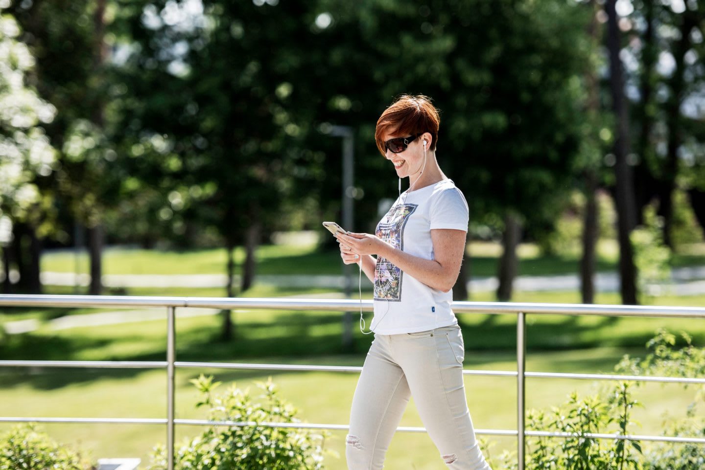 Woman in white t-shirt walking outdoors while looking at phone, nature, green, break