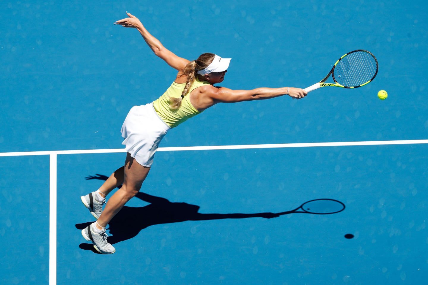 Woman wearing a yellow and white tennis outfit hitting a tennis ball with a racket on a blue court, Caroline Wozniacki, tennis, player, Danish, athlete, adidas, Australia, Melbourne