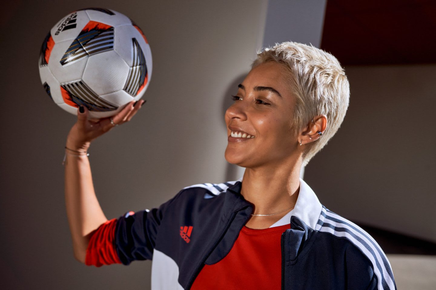 Woman with blonde short hair wearing sports outfit holding football ball in hand while smiling, adidas, football, women, inclusion