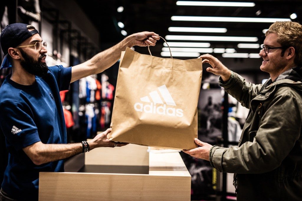 Store assistant handing over sustainable adidas brown paper bag to consumer at cashier, adidas, store, retail. sustainable, sustainability
