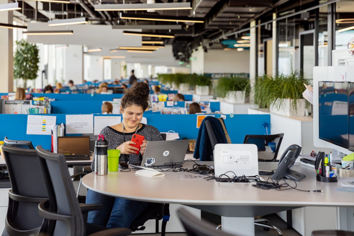 Woman looking at mobile phone in front of laptop in an open office, adidas, employee, workplace, happy, people