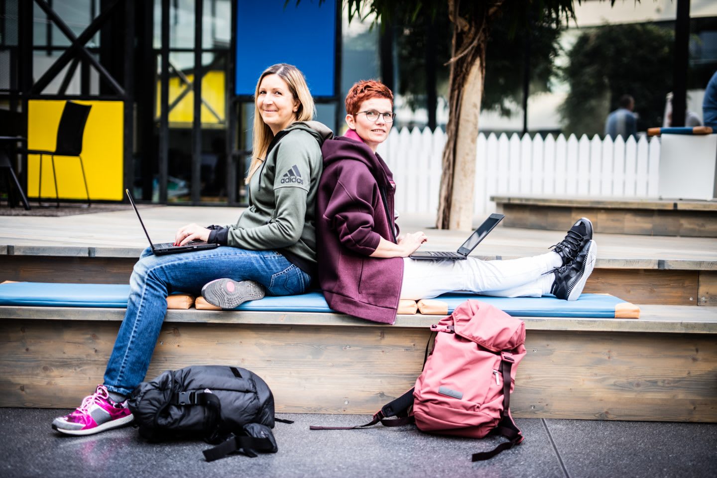 Two Women sitting back to back holding laptops job sharing interview at adidas