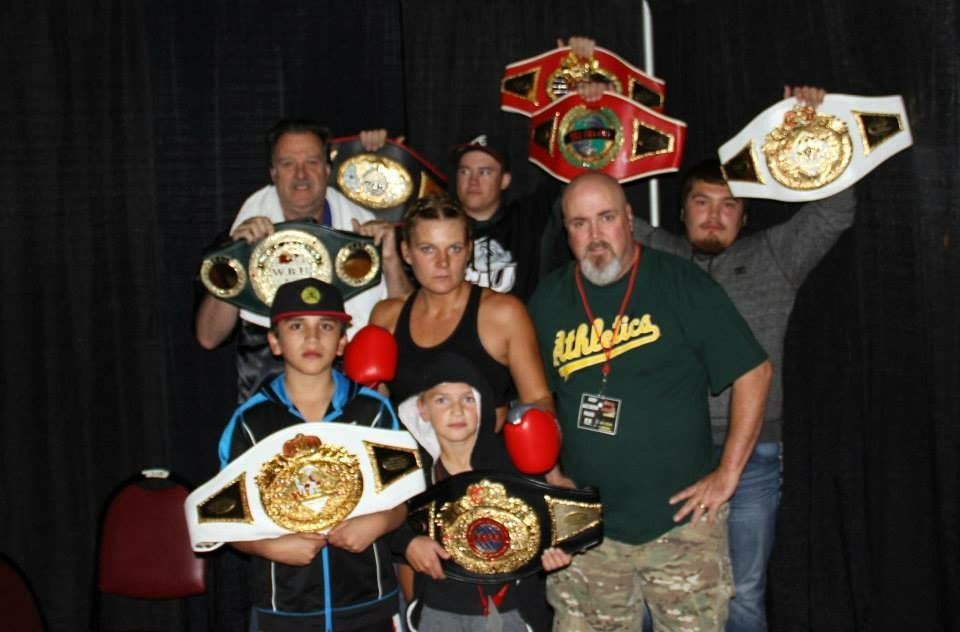 Lisa Garland is in fighting stance, surrounded by friends and family holding up her championship belts. Motivation; win; fight; boxing; GamePlanA; adidas; Goals; Dream; Role Model