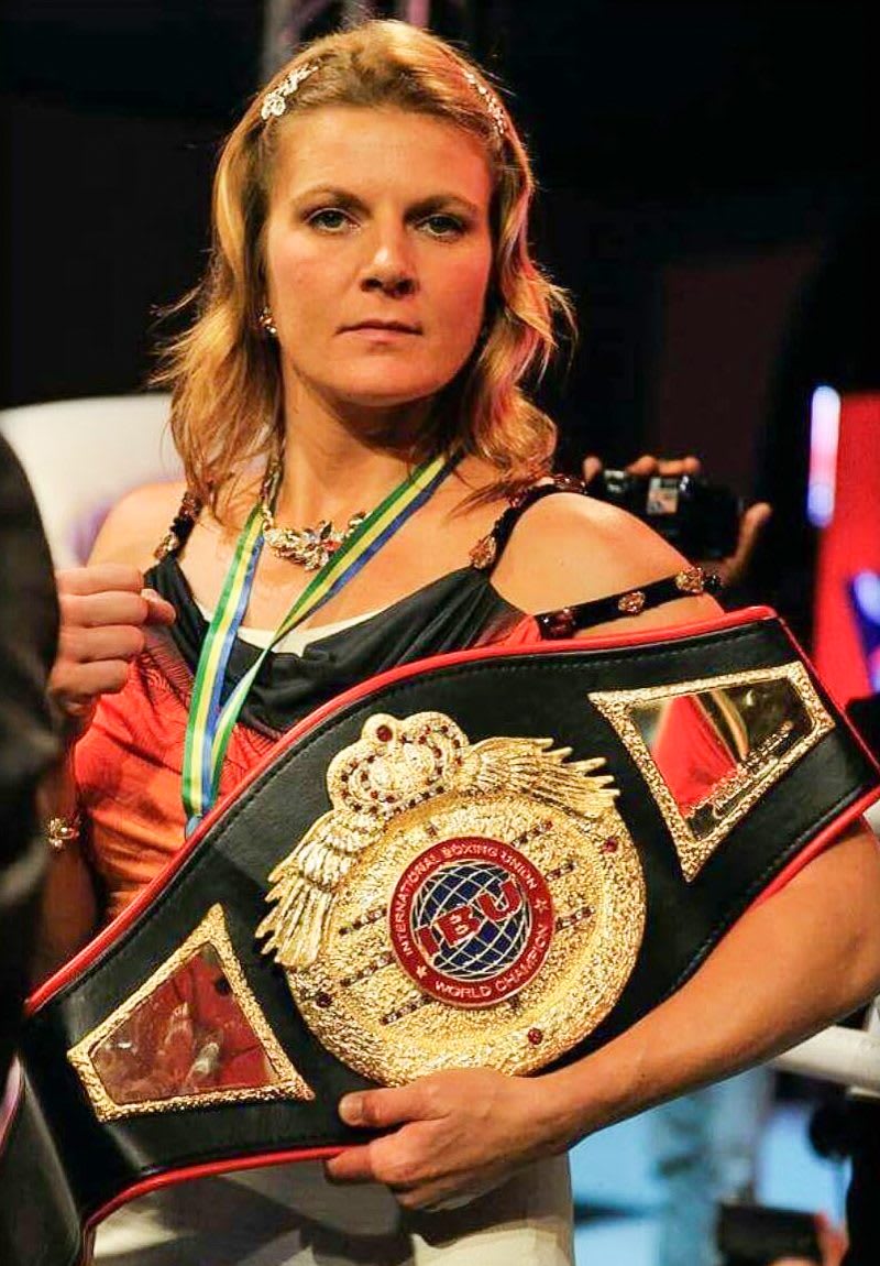 Lisa Garland is facing the camera, holding one of the belts she won in boxing. Motivation; GamePlanA; Goals; Champion; Feminine; Hard work; Boxing