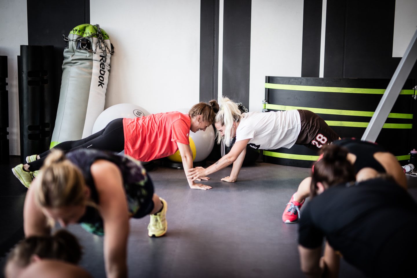 A group of people are in plank position during a workout while two women are seen performing the exercises as partners. Workout; Fitness; Gym; Motivation; Dedication; Teamwork; Partner; Reebok; Adidas; GamePlan A