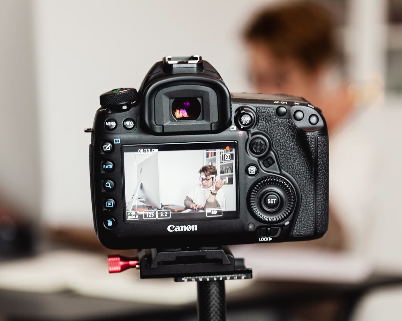 A camera on a tripod filming a scene of someone sitting at their desk.