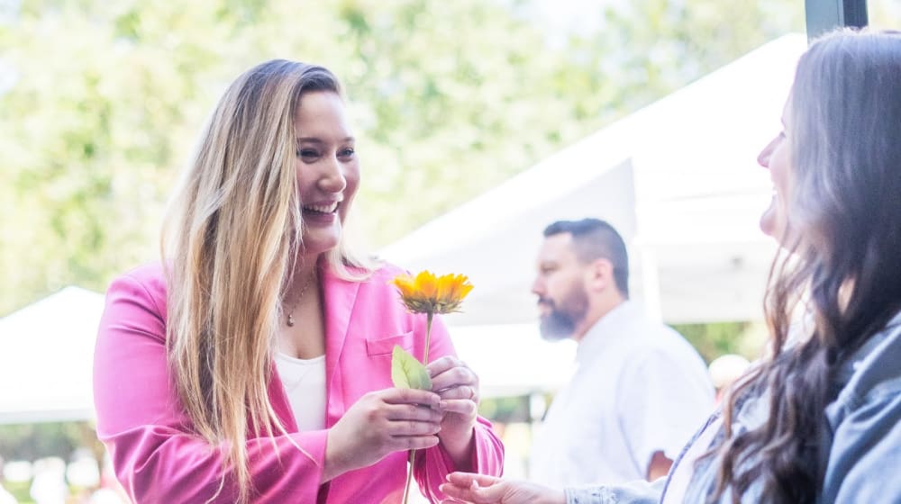 A woman warmly handing a fresh sunflower to a newcomer