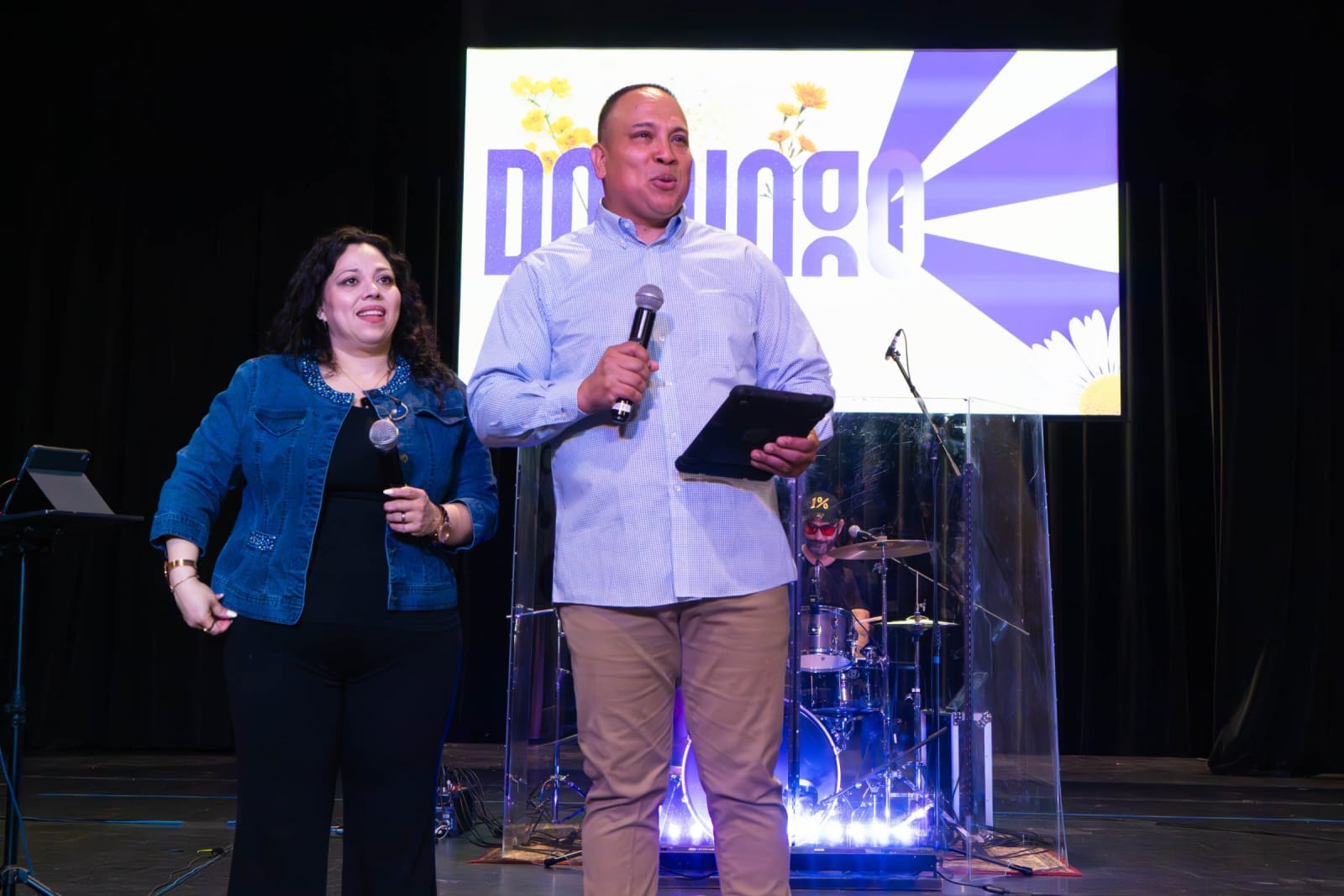 Hosts speaking on stage at a service / grayson