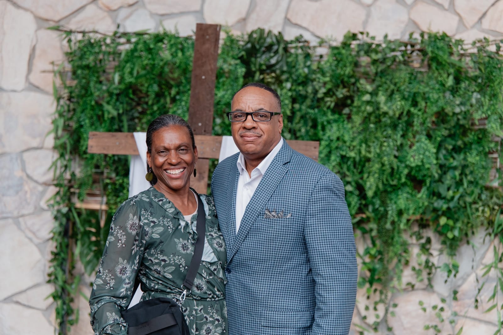 smiling couple posing in front of a greenery wall / gwinnett
