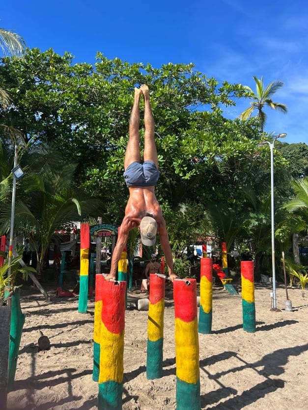 coach de movimiento realizando handstand en paralelas en un gimnasio al aire libre junto al mar