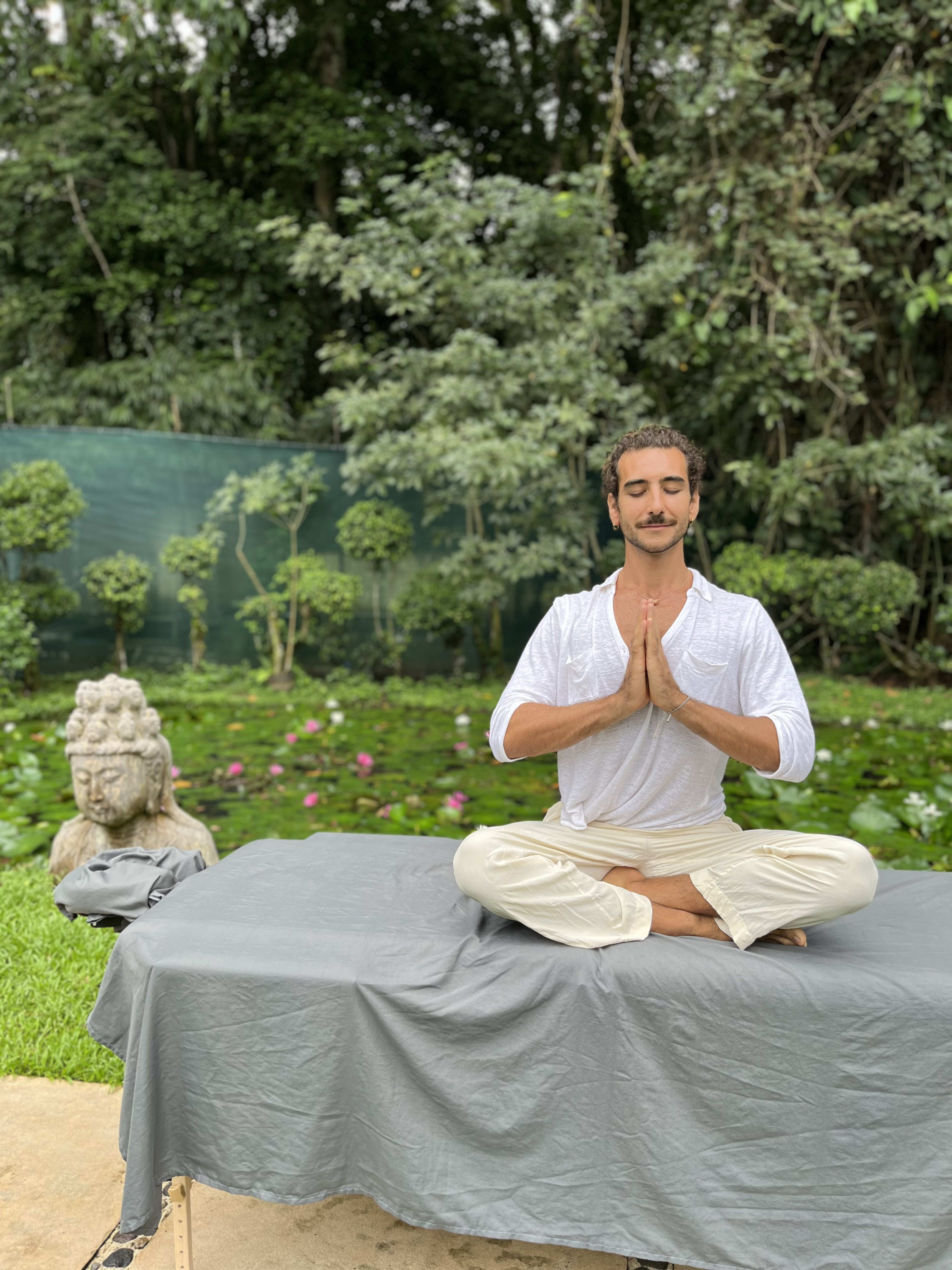 Coach con los ojos cerrados en posición de loto con manos juntas sobre el pecho en un jardín zen